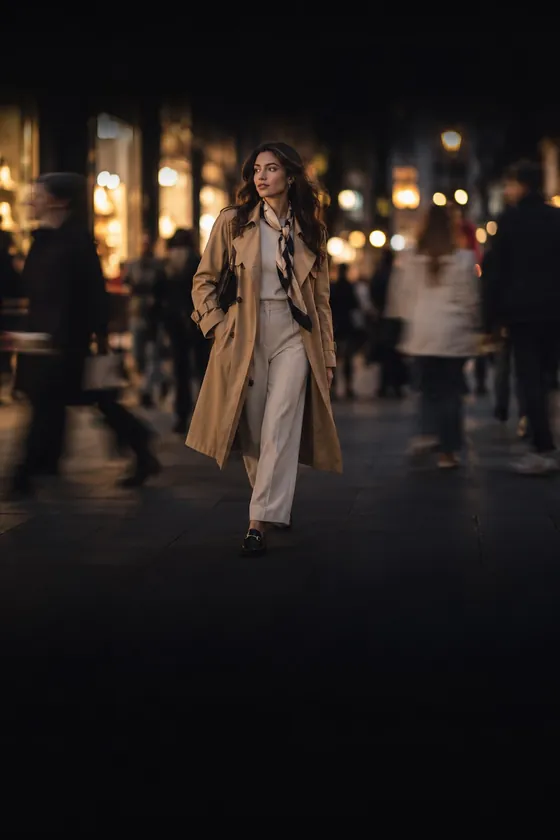 A woman in a camel trench coat walking through a busy street at night